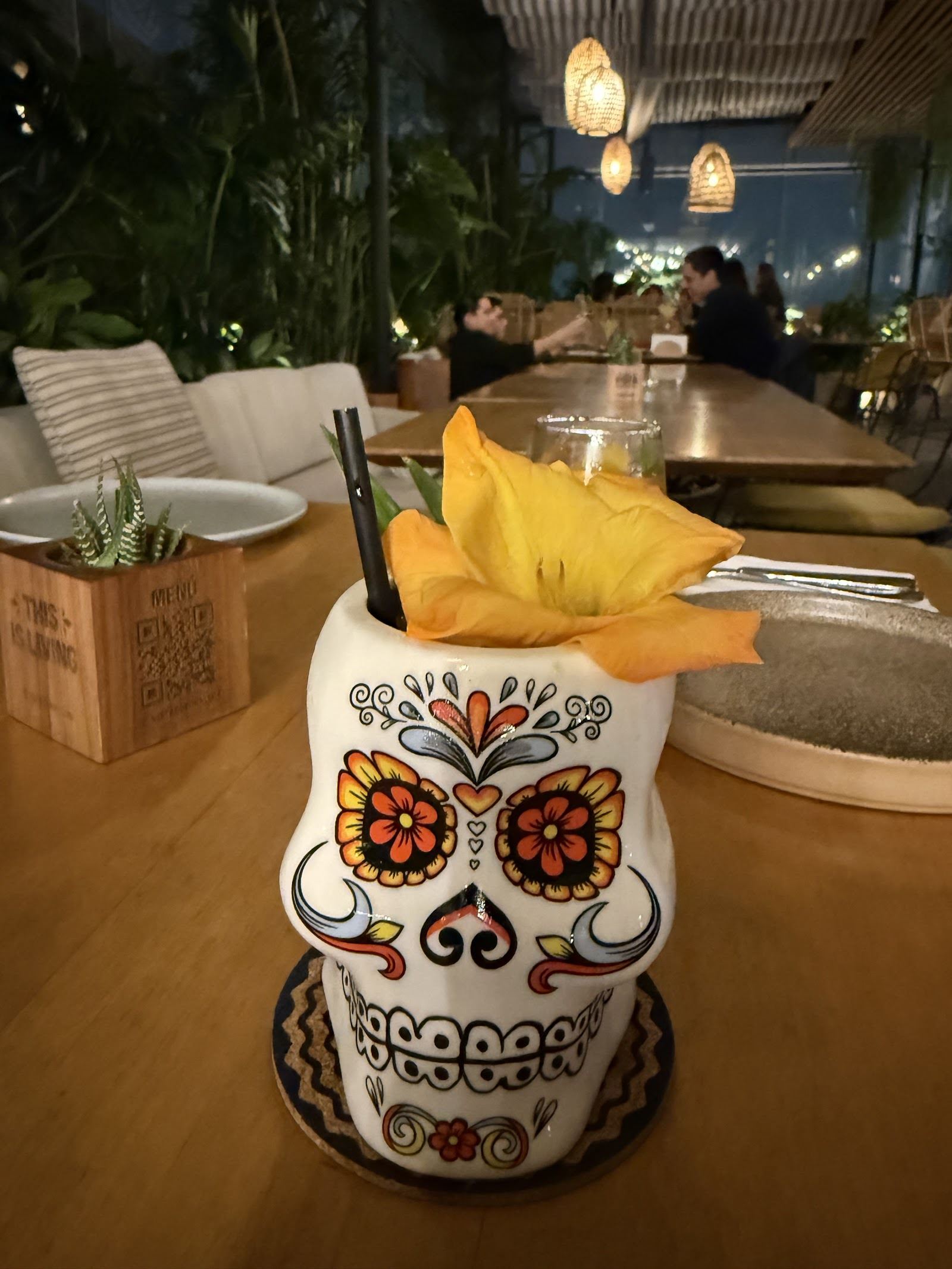 Cóctel servido en taza de calavera mexicana con flor amarilla, en ambiente nocturno